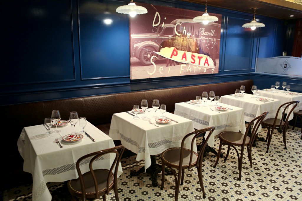 A view of the dining room at Carbone NYC featuring a large piece of mural art on the walls. 