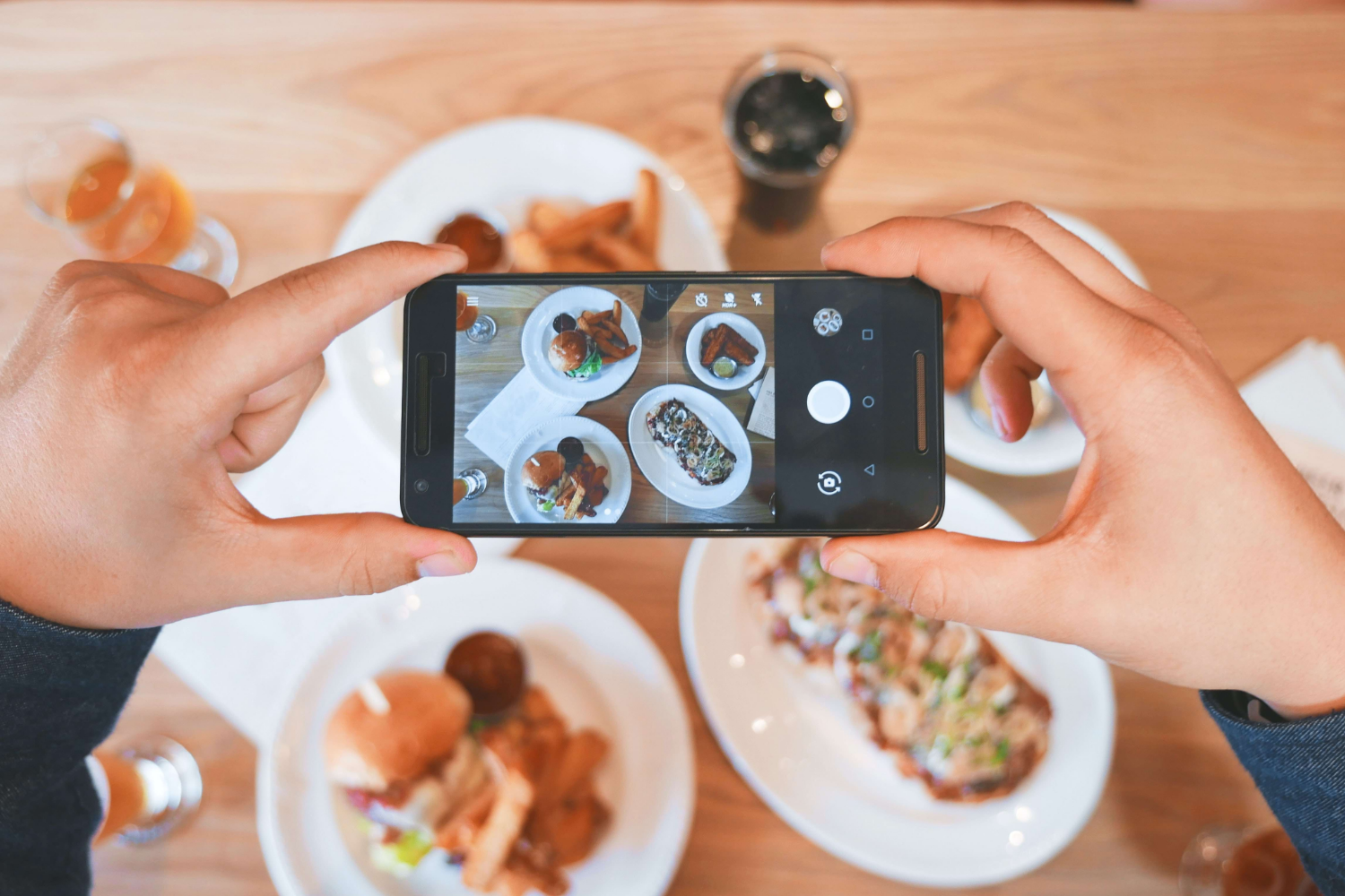 A person holding an iphone over a dining table full of dishes, getting ready to create their own UGC.