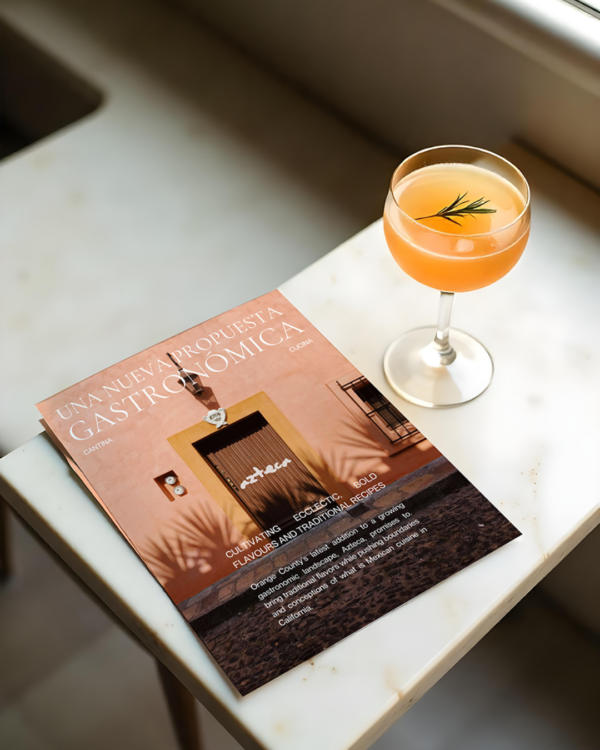 A mockup of a promo card in the Azteca brand style sitting on a marble counter next to an orange cocktail.