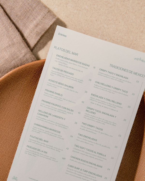 A mockup of a menu in the Azteca brand style sitting on top of a terra cotta clay plate.