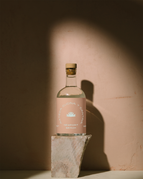 A bottle of tequila with a label featuring the Azteca logo on mauve tone background with dark shadows.