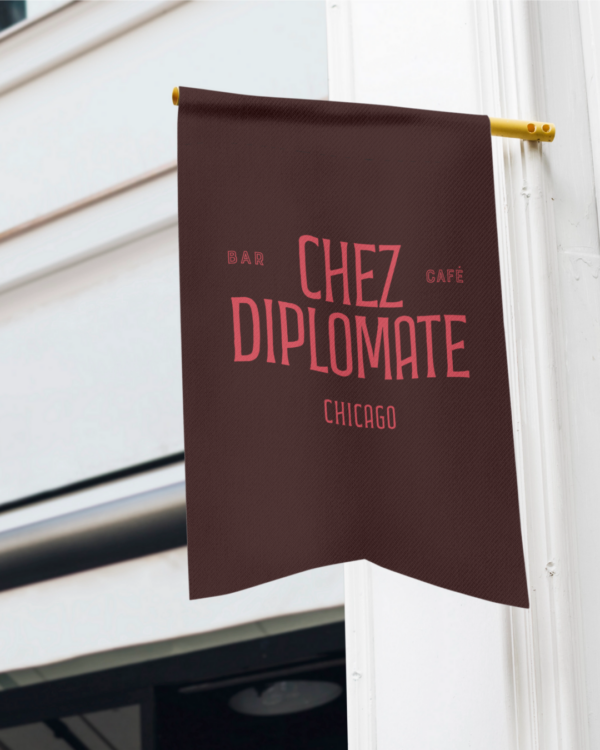 A close up of a burgandy flag outside of a white building featuring the red "Le Diplomate" logo on the front.