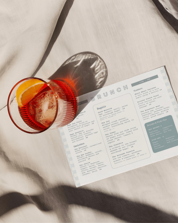 A close up of a white and sage-green menu with a negroni cocktail sitting on the top corner.